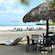 Tables with a mix of thatched roof and modern umbrellas line a beach that has palm trees